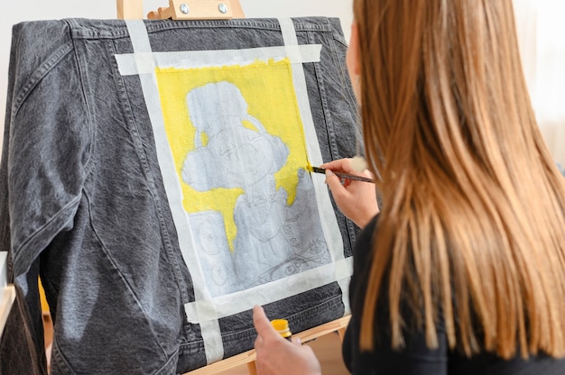 Designer drawing on a denim jacket woman with a brush creating personal art on jeans working in a