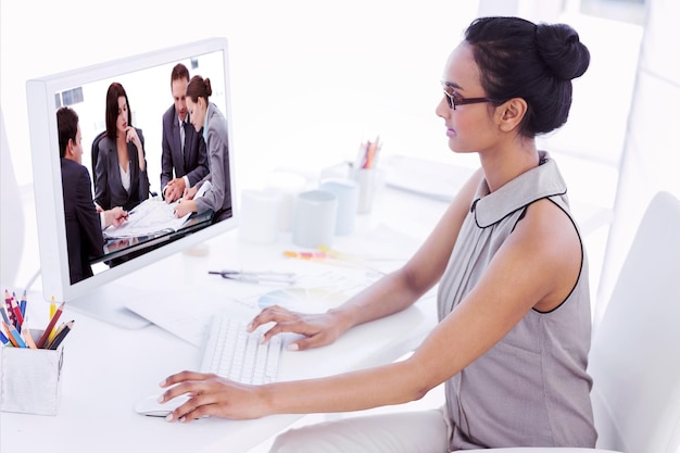 designer working at her desk using computer against four serious engineers looking at plans sitting at a table