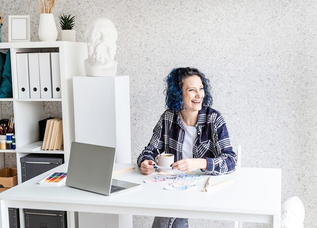 Designer working with colour palettes and laptop in her art studio