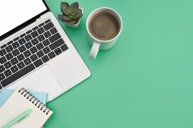 Designer workplace with laptop computer coffee cup and notebook on green background Top view