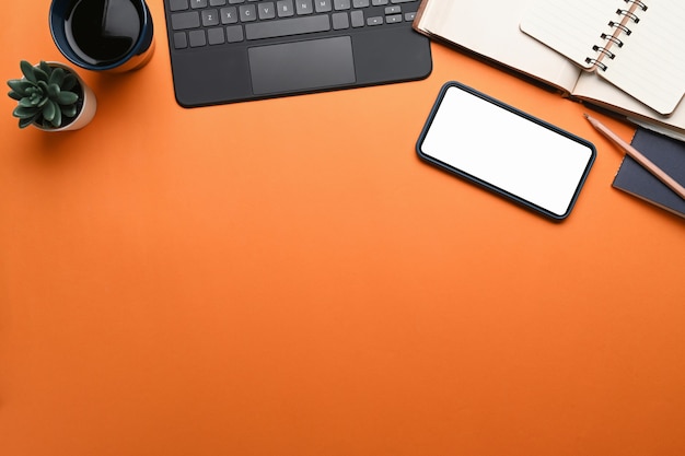 Designer workplace with smart phone, keyboard, notebook and copy space on orange background.