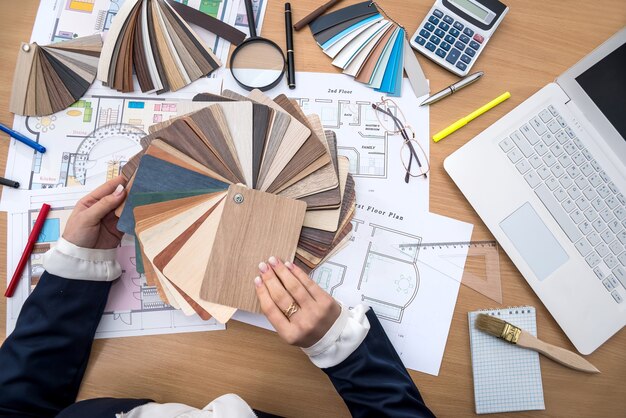 designer works in the office with samples of colors, a laptop and a plan of the building