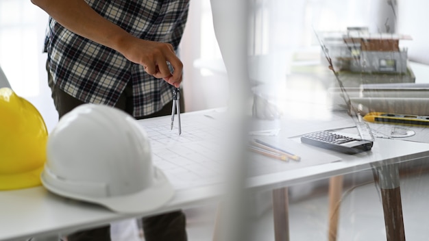 Designers use compasses to draw designs on house plans, House plans, and safety helmets with drawing tools on the table.