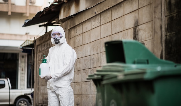 Desinfectie specialist man in persoonlijke beschermingsmiddelen (pbm) pak, handschoenen, masker en gelaatsscherm, reiniging quarantainegebied met een fles onder druk staand desinfectiemiddel om coronavirus te verwijderen