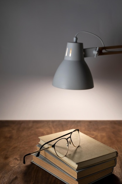 Desk lamp illuminates the workplace on the office desk stack of books and glasses