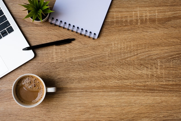 Desk office with laptop, blank notebook and coffee cup on wooden table