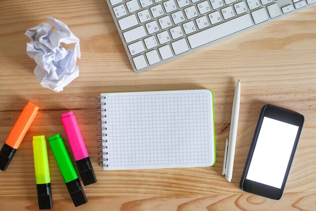 A desk with a keyboard, a notebook, a pen, and a pen on it.