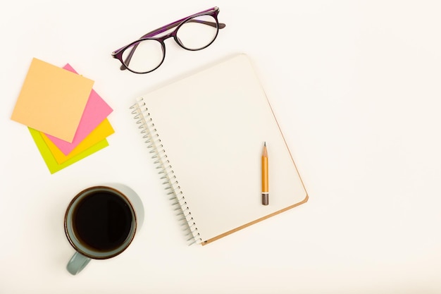 A desk with a notebook, glasses, a pen, and a cup of coffee