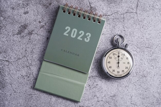 Desktop calendar 2023 and stop watch on cement background