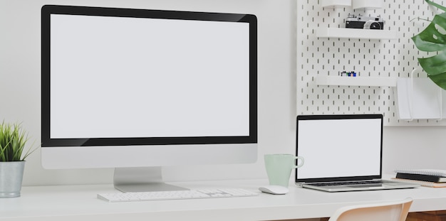 Desktop computer and blank screen laptop with copy space and office supplies in minimal white office room.