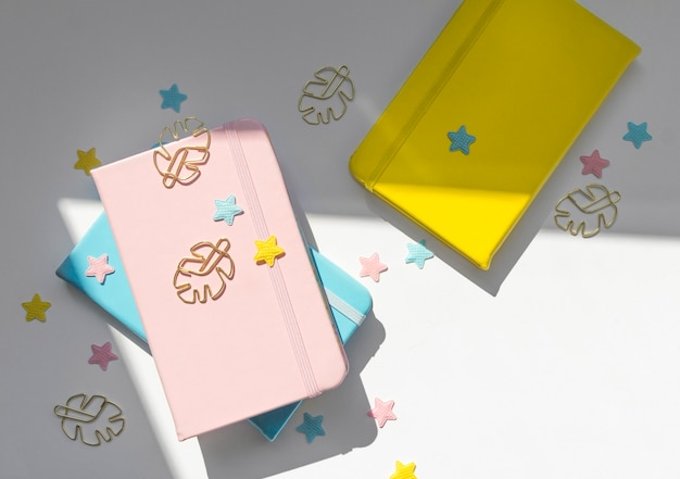 Desktop feminine flat lay composition with pink, yellow and blue notepads, stars and monstera golden clips