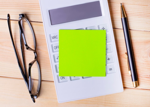 The desktop has a green blank sticker with a place to insert text a calculator glasses and a pen Top view of the workplace Copy space