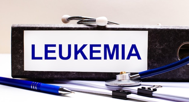 На рабочем столе есть стетоскоп, синяя ручка и серая папка с текстом LEUKEMIA Medical concept