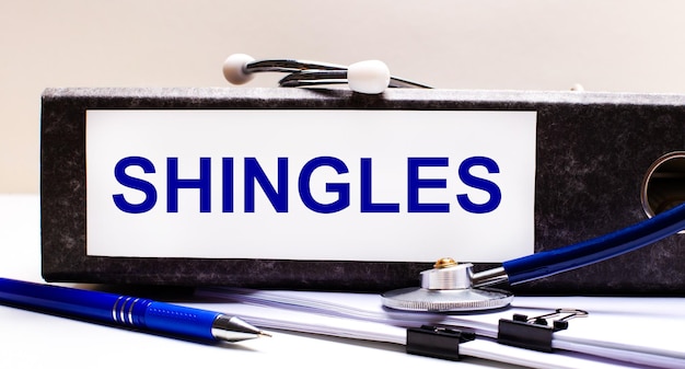 데스크탑에는 SHINGLES Medical 개념이라는 텍스트가 있는 청진기, 파란색 펜 및 회색 파일 폴더가 있습니다.