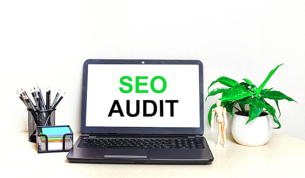 On the desktop is a potted plant stationery and an open laptop with the text SEO AUDIT on the screen Home Office