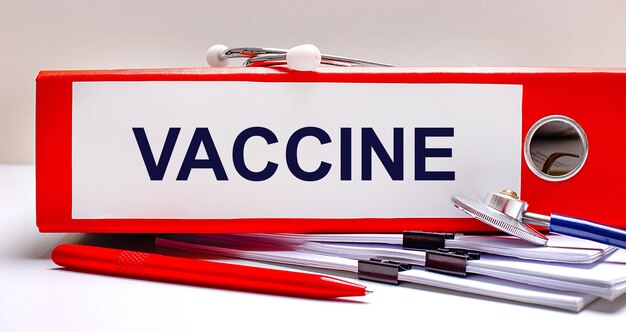 Sul desktop c'è uno stetoscopio che documenta una penna e una cartella di file rossa con il testo vaccine medical concept