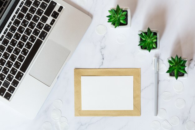 Desktop items: laptop, paper card, succulent plants lying on desk. Top view