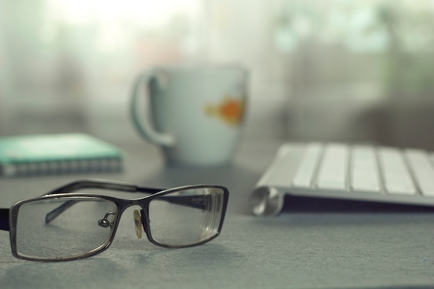 Desktop. Keyboard, glasses and a cup.