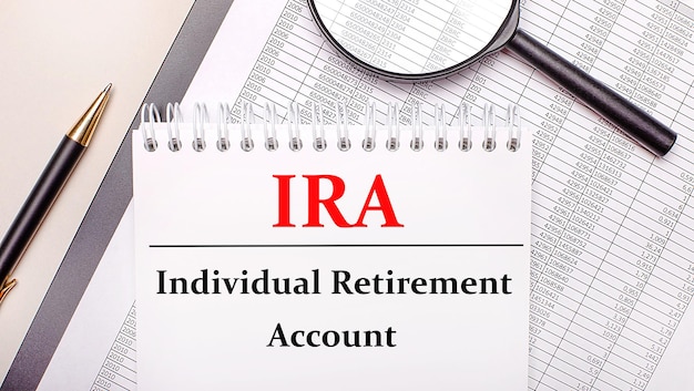 Desktop magnifier, reports, pen and notebook with text IRA Individual Retirement Account. Business concept