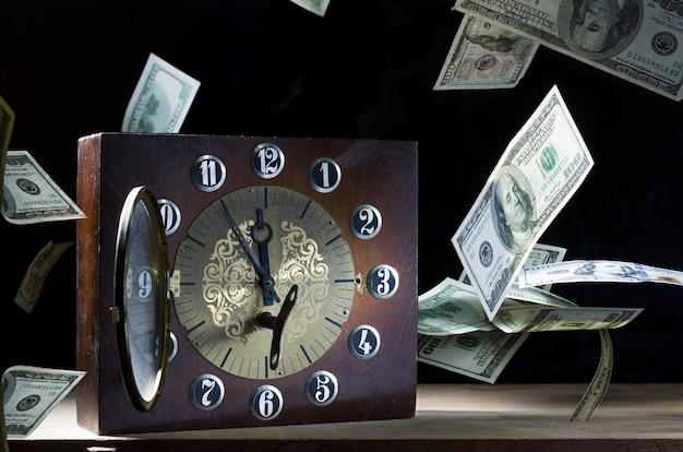 Photo desktop mechanical clock and money clock with arrows and floating money leaving time valuable time front view