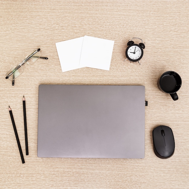 Desktop for student or freelancer. Working space. Workplace with grey modern laptop, cup of coffee, glasses and clock for time control on light table. Flat lay.