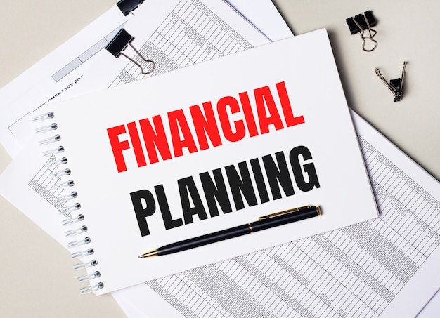 On the desktop there are documents, pen, black paper clips and a notebook with the text FINANCIAL PLANNING. Business concept