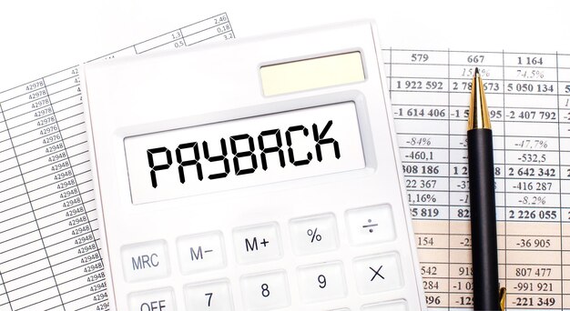 デスクトップには、レポート、スコアボードにPAYBACKというテキストが表示された白い電卓とペンがあります。ビジネスコンセプト。