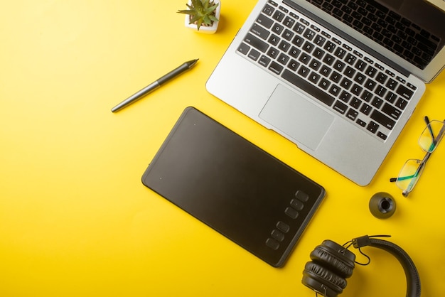 Desktopontwerper en creatieve retoucher met een grafisch tablet-laptopbril Ontwerp plat op een gele achtergrond