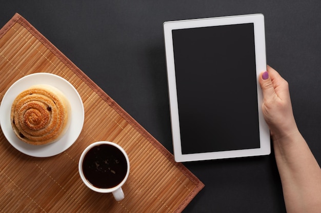 Desktopsnack van een broodje en koffie een tablet in een vrouwelijke hand