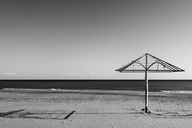 海沿いの裸の日傘のある荒涼としたビーチ。白黒写真、風景-海景