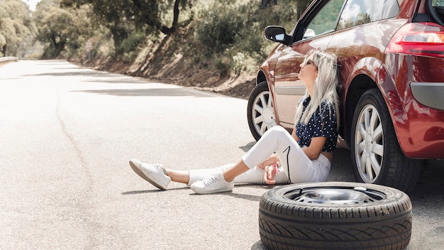 写真 道に壊れた車の近くに座っている絶望的な女性