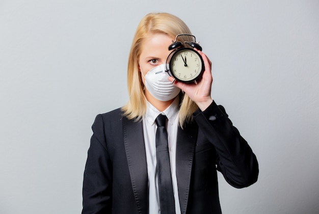 Desperate businesswoman in black suit and face mask holds alarm clock