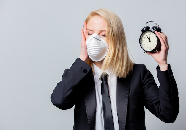 Desperate businesswoman in black suit and face mask holds alarm clock