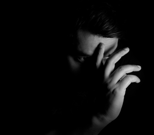 Desperate man close up portrait with long shadow on black background lowkey