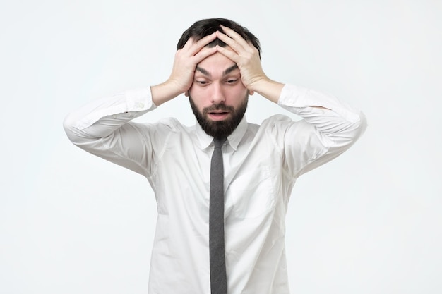 Desperate stressed young european man looking at camera in terror and shock holding head