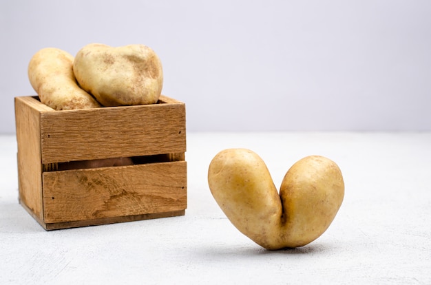 Despicable potatoes of different shapes in a wooden box, copy space.