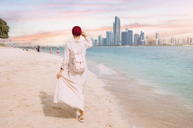 Despite the size and grandeur of the skyscrapers the woman seems undaunted as she walks confidently along the shoreline perhaps lost in thought or simply enjoying the peaceful moment