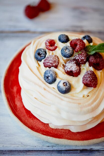 Dessert Anna Pavlova with raspberries and blueberries on white wooden surface