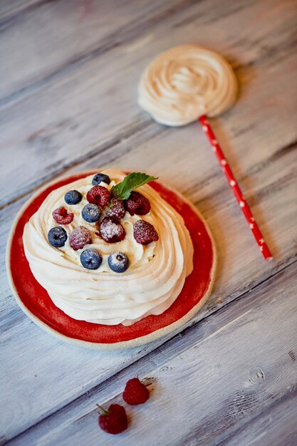 Dessert Anna Pavlova with raspberries and blueberries on white wooden surface