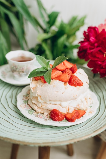 Foto torta da dessert con crema e fragole sullo sfondo di piante domestiche su un piccolo tavolo