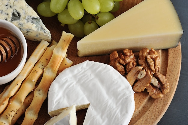 Dessert   cheese, bread sticks, honey, nuts and grapes on wooden board