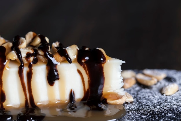 Dessert cheesecake covered with caramel with chocolate and peanuts, cheesecake on an individual tray sprinkled with powdered sugar