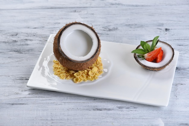 Dessert in coconut with strawberries on a white square plate, pina colada, coconut, top view