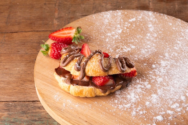 Dessert of hazelnut cream croissant with strawberry on a wooden board on a rustic table in the back