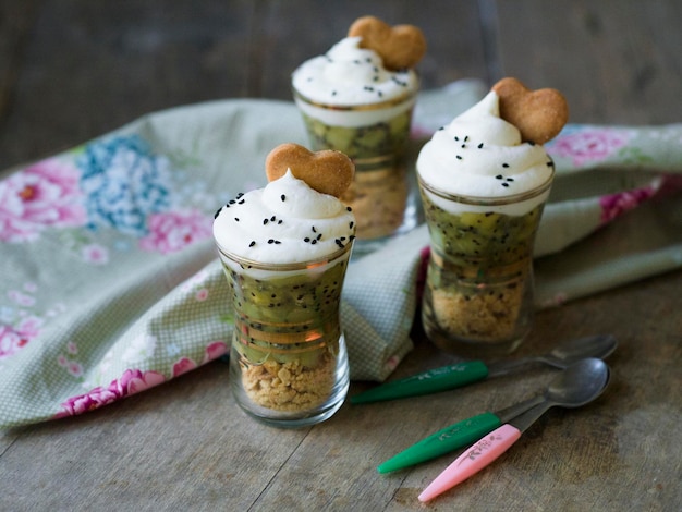 Dessert in een glas met kiwisaus witte botercrème versierd met koekjes in de vorm van een hart Dessert voor Valentijnsdag Houten achtergrond Retro bril