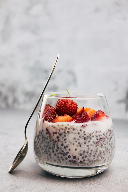 Foto dessert a base di latte senza lattosio con semi di chia e fragole in un bicchiere su sfondo grigio. cibo pulito, disintossicazione, concetto di perdita di peso. una ricetta per una dieta a basso contenuto di carboidrati.