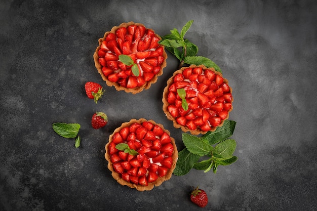 Dessert met aardbeientaartjes met room en aardbeien versierd met munt op donkere achtergrond