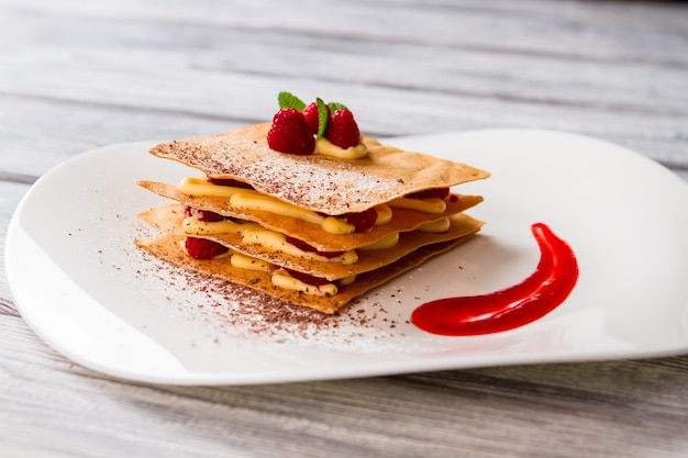 Dessert met gele vla. Bessen en chocoladepoeder. Nieuw recept van frambozen millefeuille. Smeer van fruitsaus.