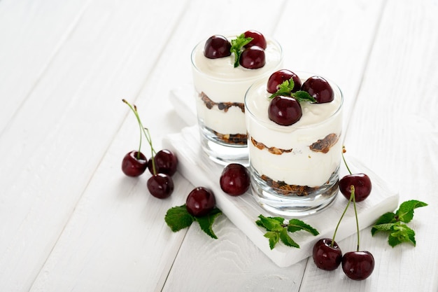 Dessert met kaas, verse kersen en muesli in een glas op een witte houten achtergrond