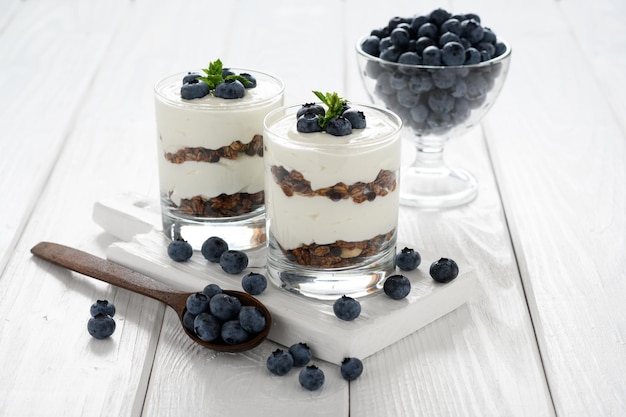 Dessert met kwark verse bosbessen en muesli in een glas op een witte houten achtergrond